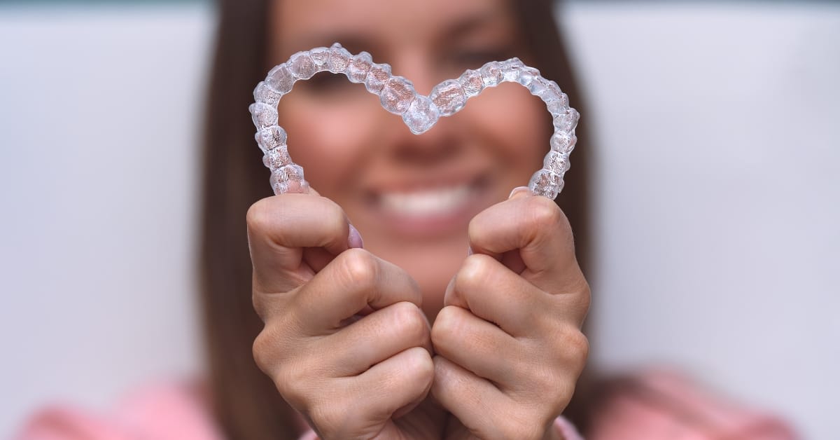 A woman is holding a heart made from Invisalign aligners.