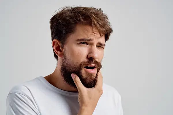 Man holding jaw in pain from TMD temporomandibular disorder symptoms