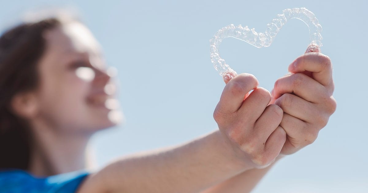 Image of a girl holding two invisible aligners in the shape of a heart