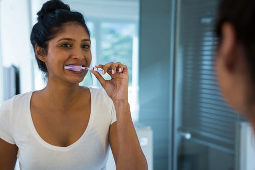 Young woman brushing her teeth while looking in the mirror Young woman brushing her teeth while looking in the mirror
