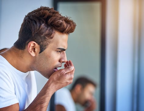 Man checking his breath by cupping hand over mouth for bad breath detection