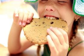 Child eating sugary cookie representing simple carbs that can harm teeth