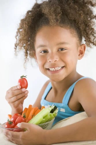 Young girl smiling while eating vegetables