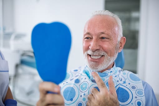 Older patient at dentist appointment looking into a and mirror and gesturing towards his face